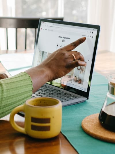 Person uses laptop at breakfast table with pot of coffee and coffee mug nearby.